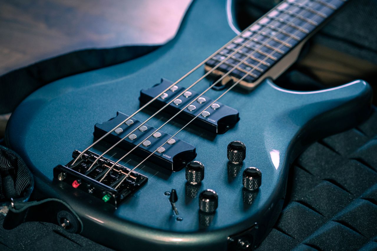 Detailed view of a dark blue electric bass guitar showcasing strings and controls in soft lighting.